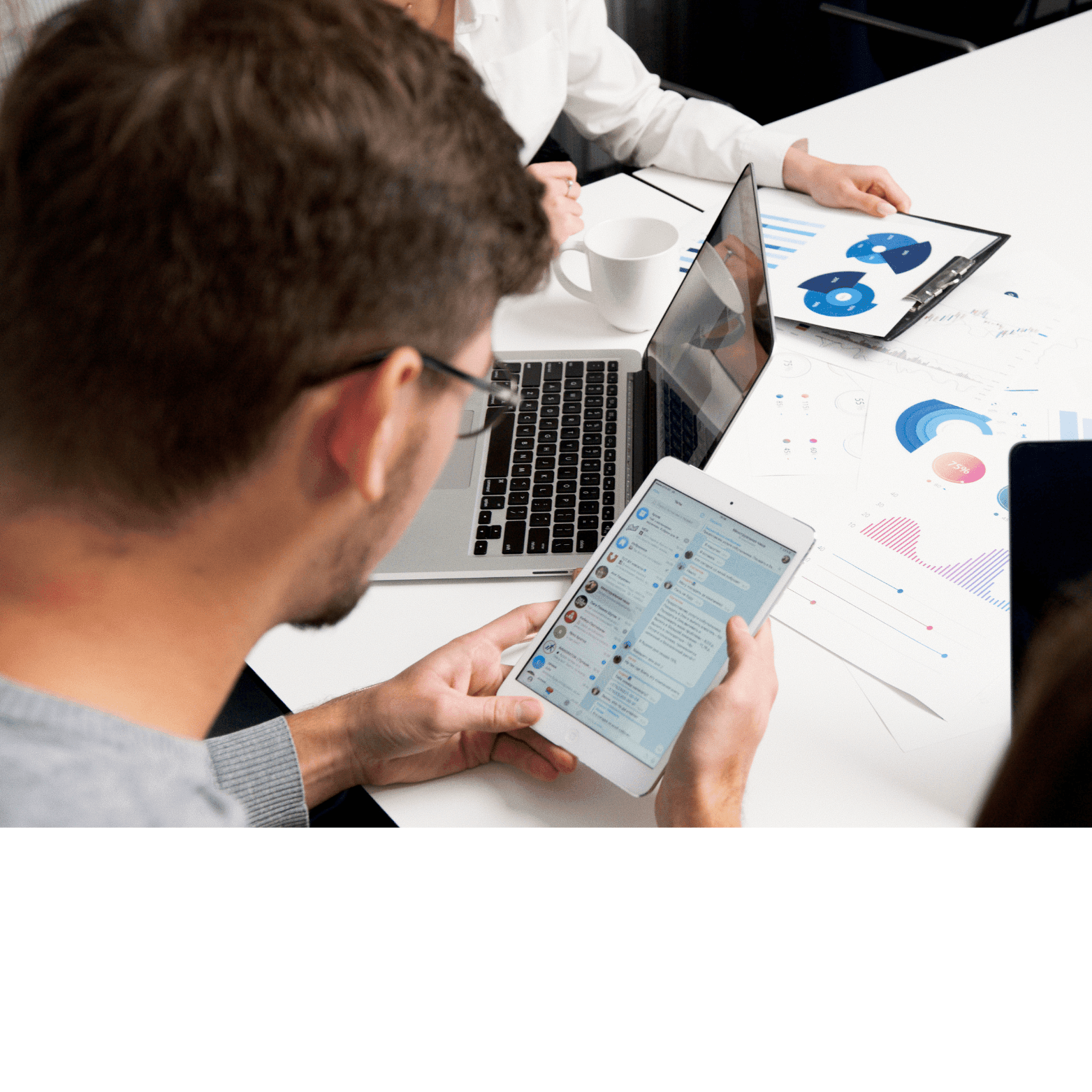 People working at a table with laptops, a tablet, and paper charts displaying data and graphs.