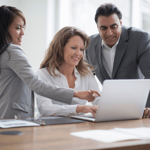 Three business professionals collaborating around a laptop in a modern office setting.